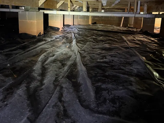 Bare dirt showing through torn black plastic in an unsealed crawl space