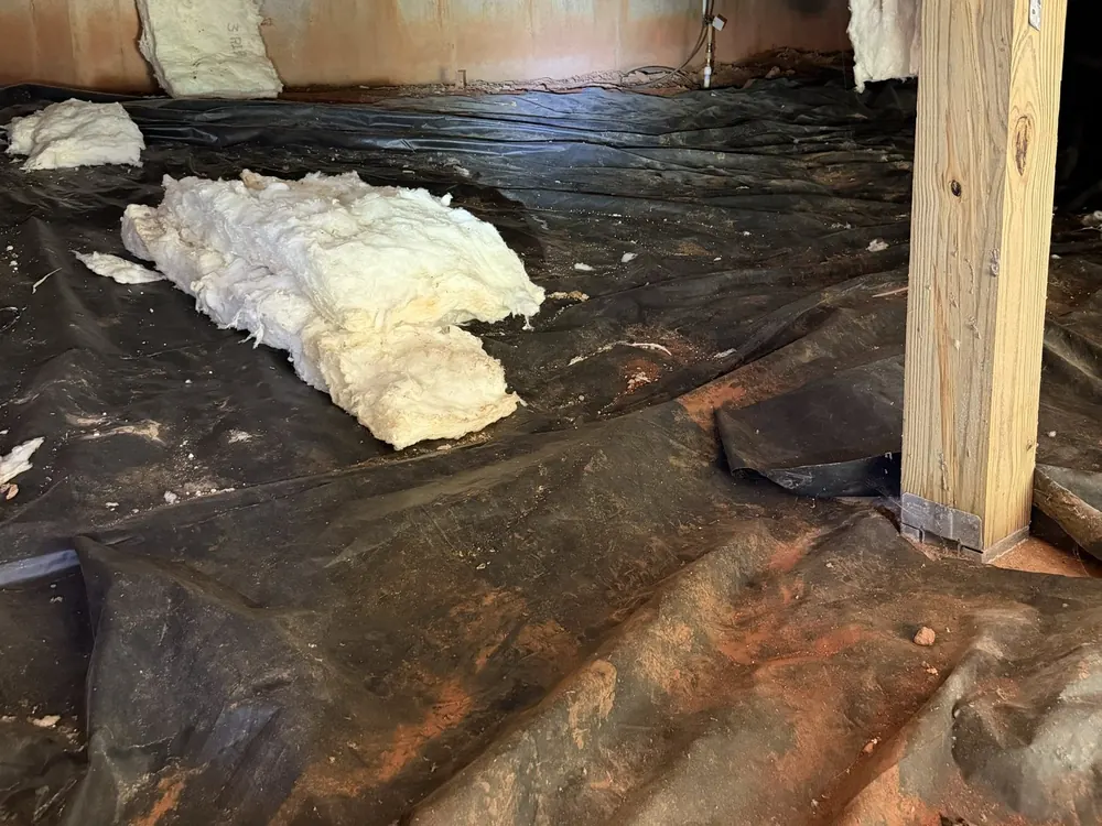 Dirty, torn black plastic and loose insulation across a crawl space floor