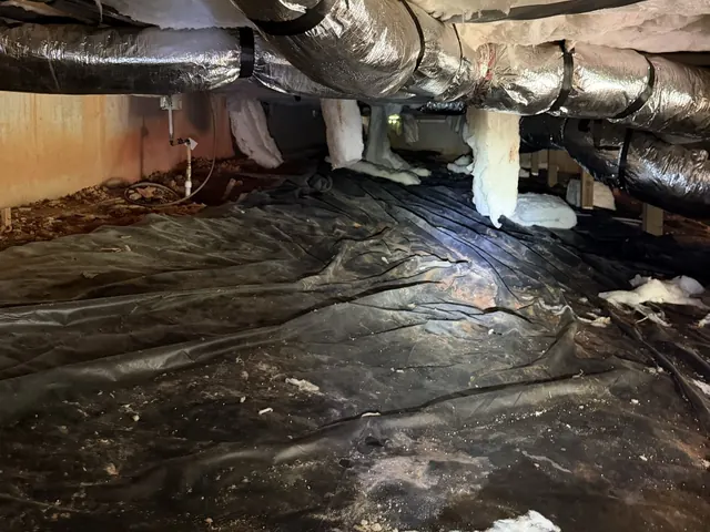 Rusted, soaked black plastic and fallen insulation in a crawl space before Crawl Space Doctors went to work