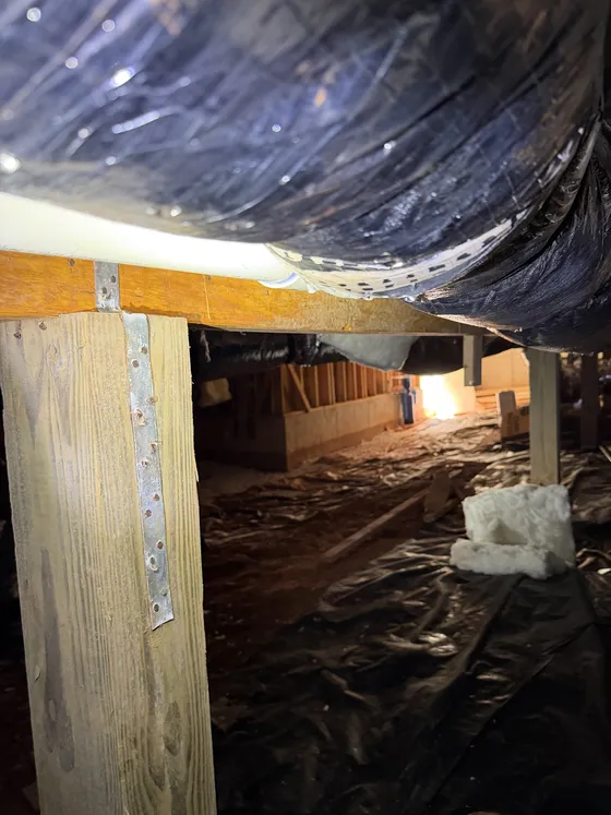 Crawl space before: a dark, torn vapor barrier under wood beams